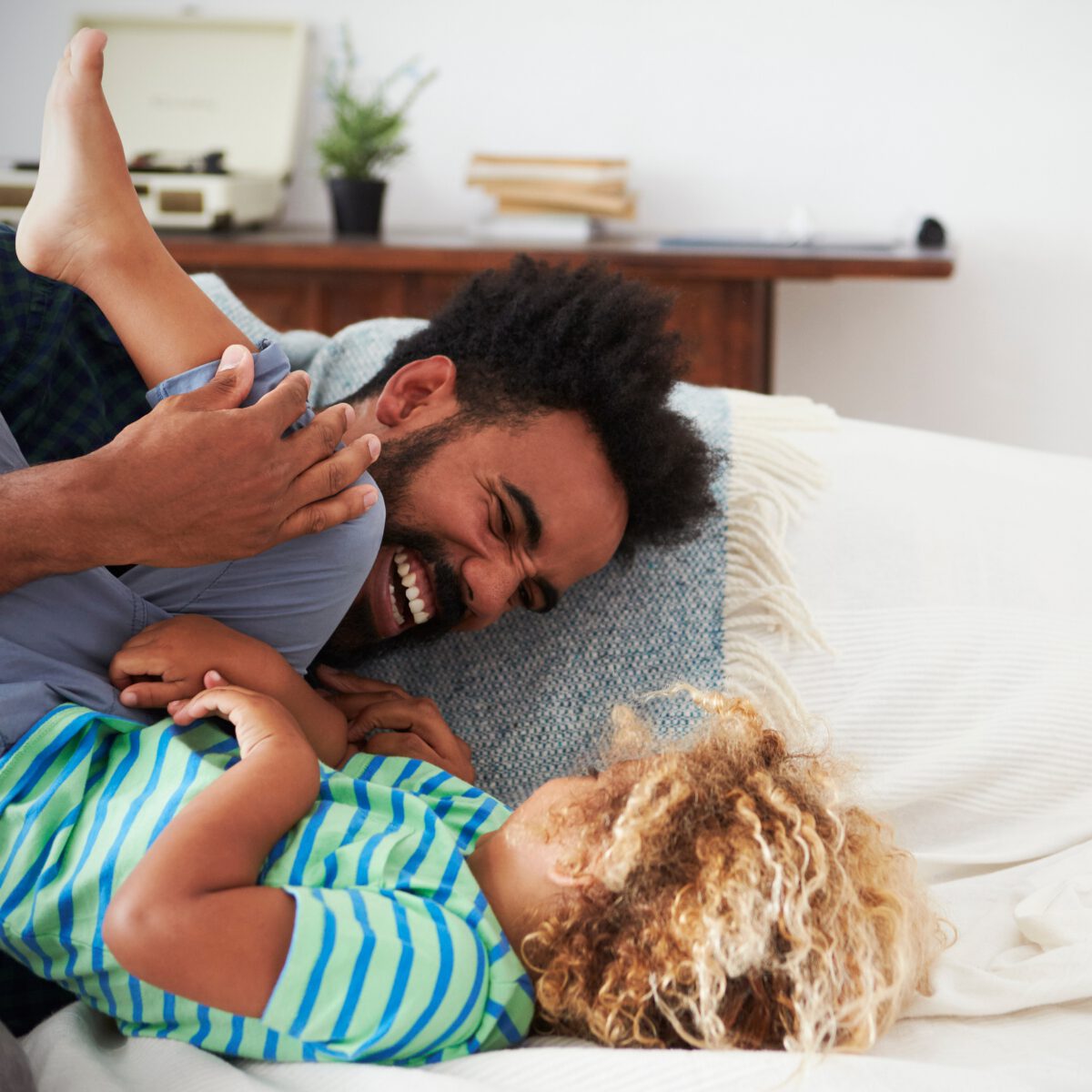 A father playing with his two young children on a bed at home.